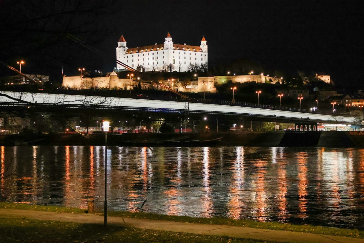Svetlá mesta sa odrážajú v Dunaji, nad mostom svieti Bratislavský hrad