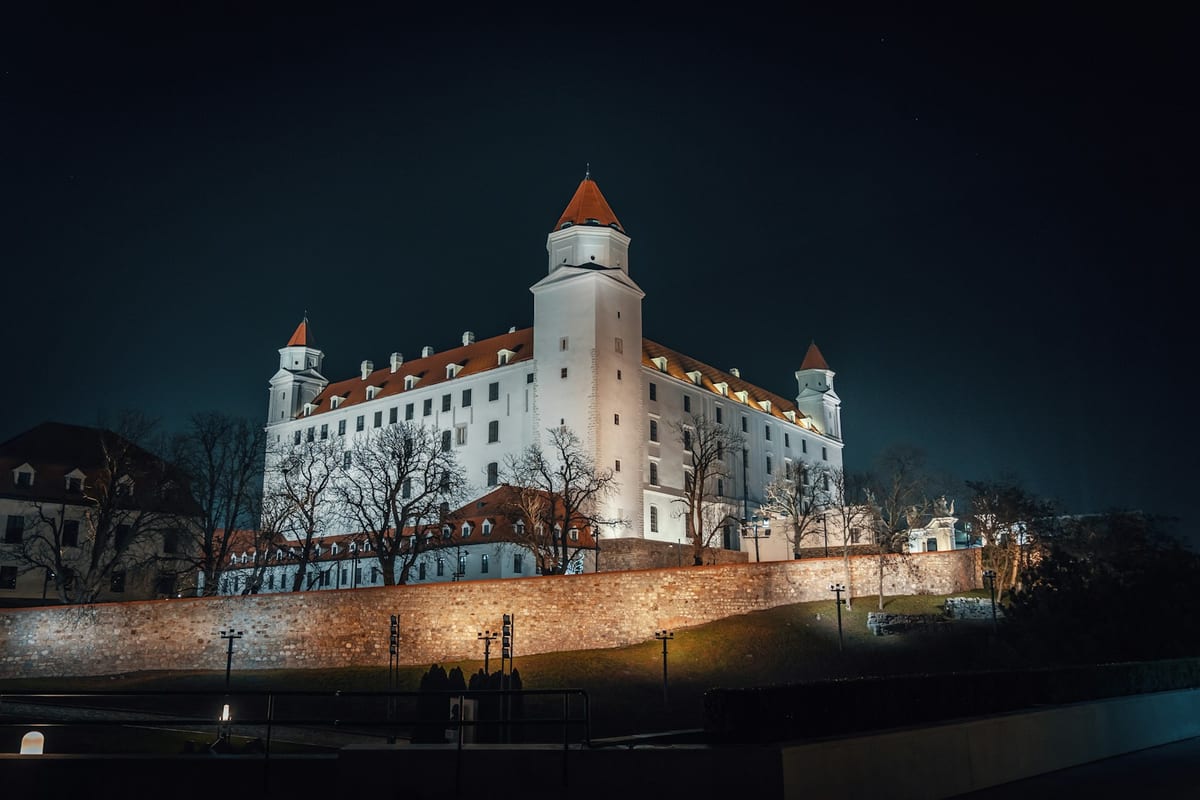 Osvetlený Bratislavský hrad v noci s ľuďmi na chodníku pod hradbami