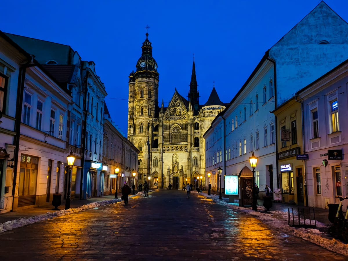 Osvetlený Dóm svätej Alžbety na konci ulice so zvyškami snehu za zimného súmraku
