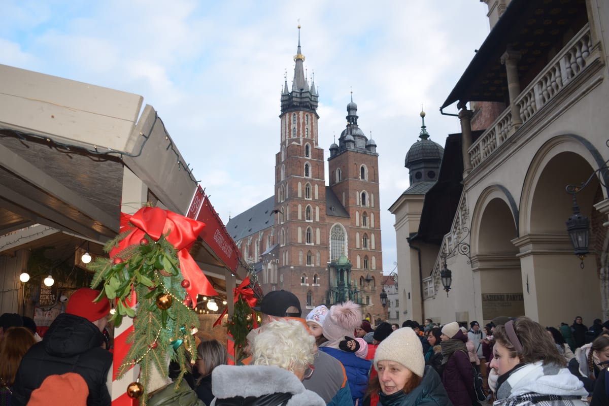Ľudia medzi stánkami na Rynku Głównom pod vežami Mariánskeho kostola