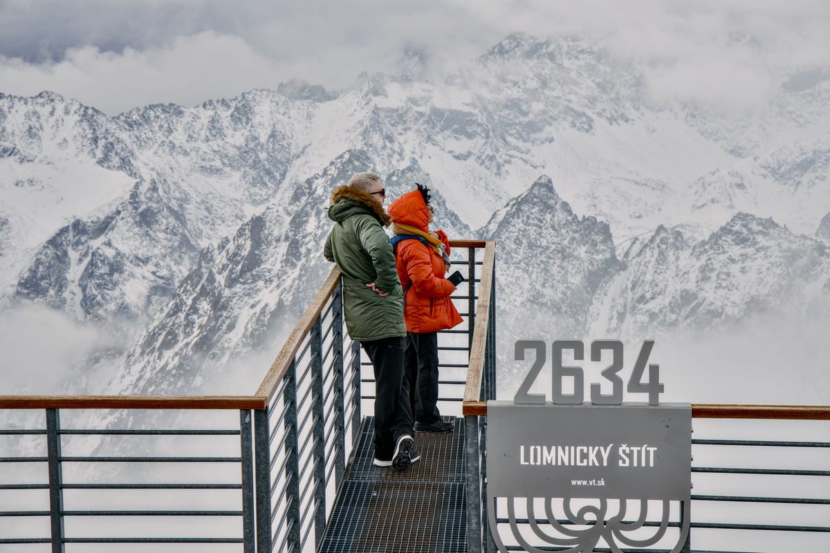 Dvaja turisti na vyhliadke Lomnického štítu vo výške 2634 m hľadia na zasnežené tatranské hrebene.