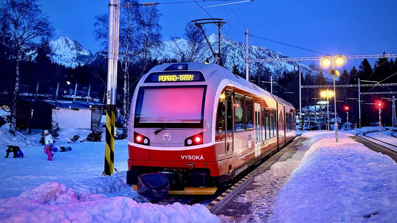 Červená tatranská električka stojí večer v snehu na Štrbskom Plese pod zasneženými štítmi