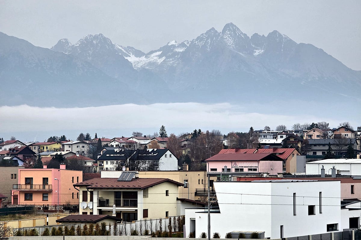 Zasnežené štíty Vysokých Tatier nad hmlou a strechami domov, výhľad od železničnej stanice Poprad-Tatry.