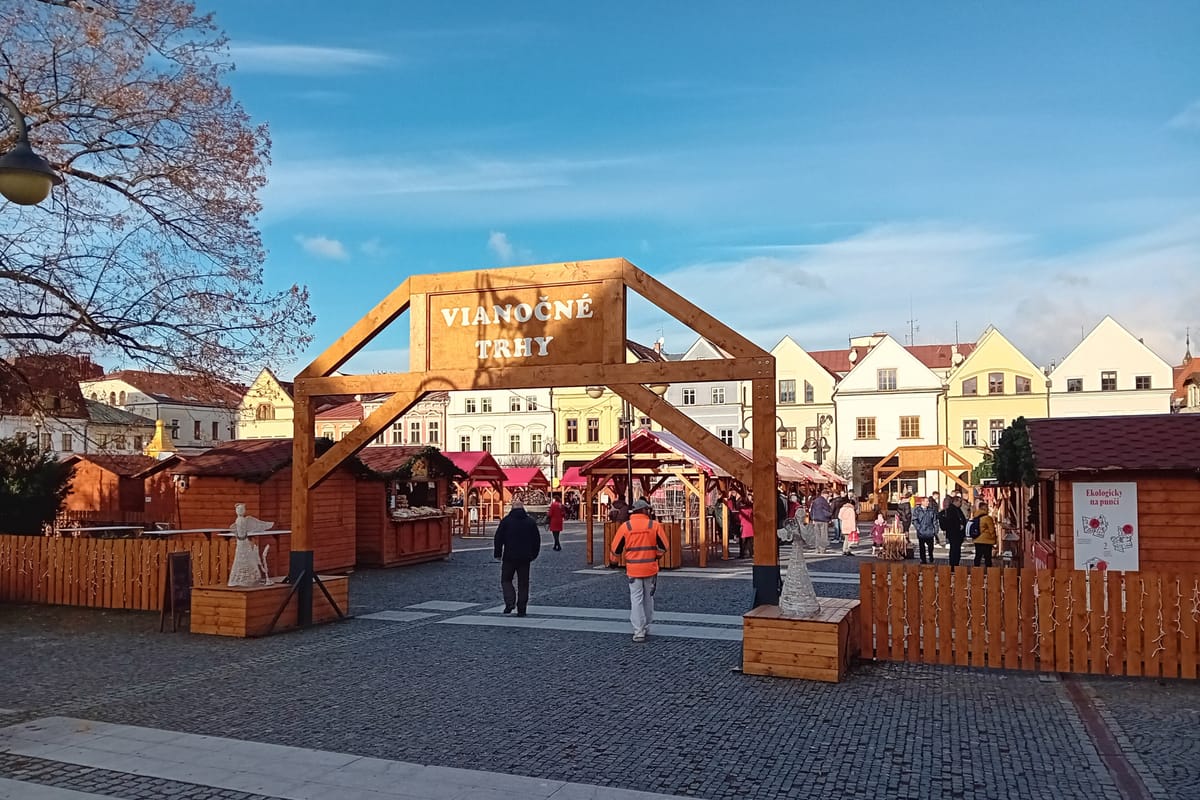 Drevená brána s nápisom Vianočné trhy a stánky na námestí za slnečného dňa