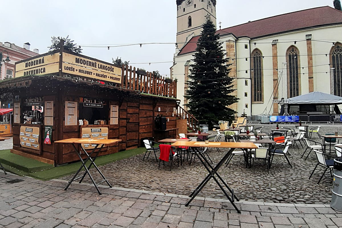 Drevený vianočný stánok s lokšami a langošmi a stoly pred kostolom