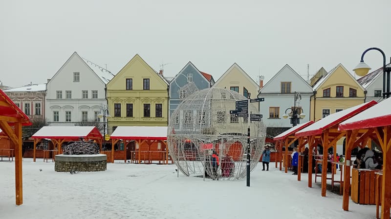Drevené vianočné stánky so snehom na námestí pred farebnými meštianskymi domami