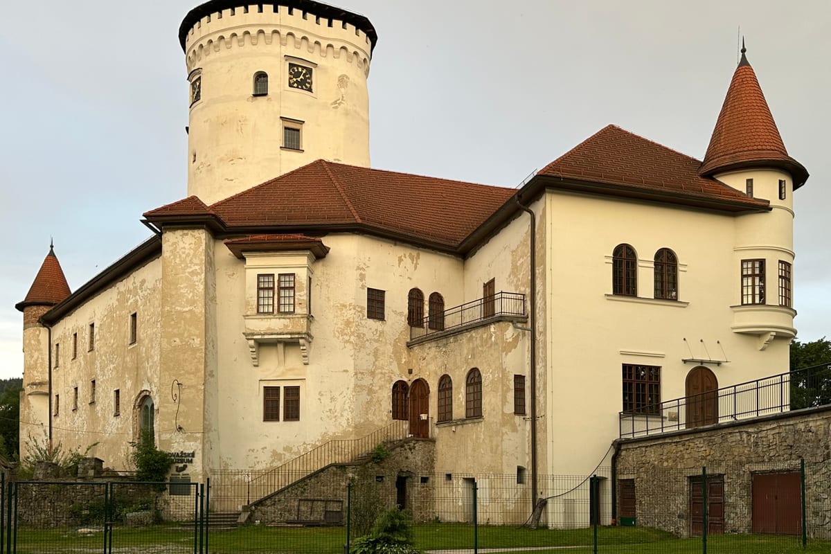 Budatínsky hrad s bielou okrúhlou vežou a červenými strechami vo večernom svetle.