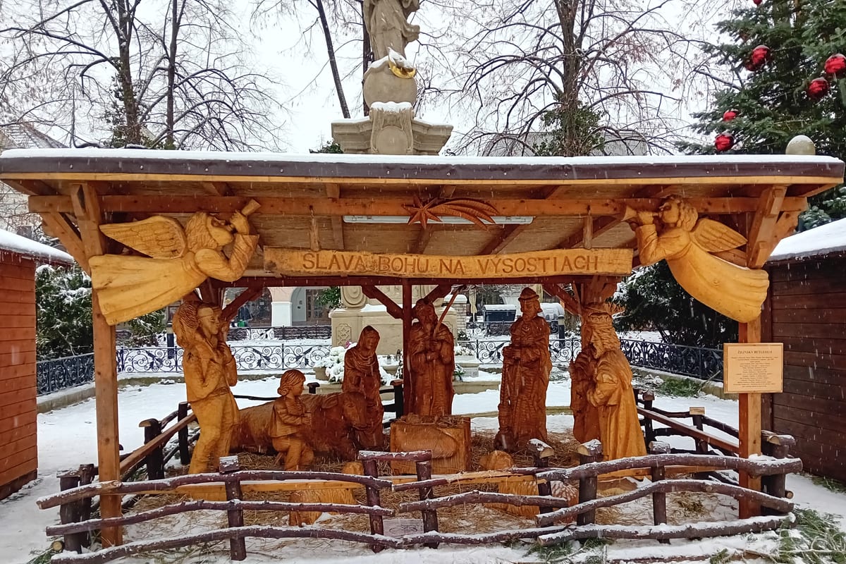 Vyrezávaný drevený betlehem s nápisom Sláva Bohu na výsostiach na zasneženom Mariánskom námestí.