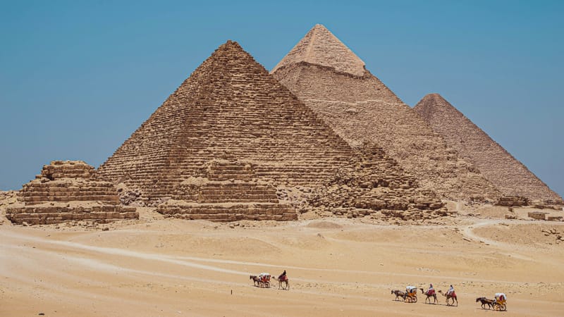 Pyramídy v Gíze na okraji púšte a jazdci na koňoch pred nimi