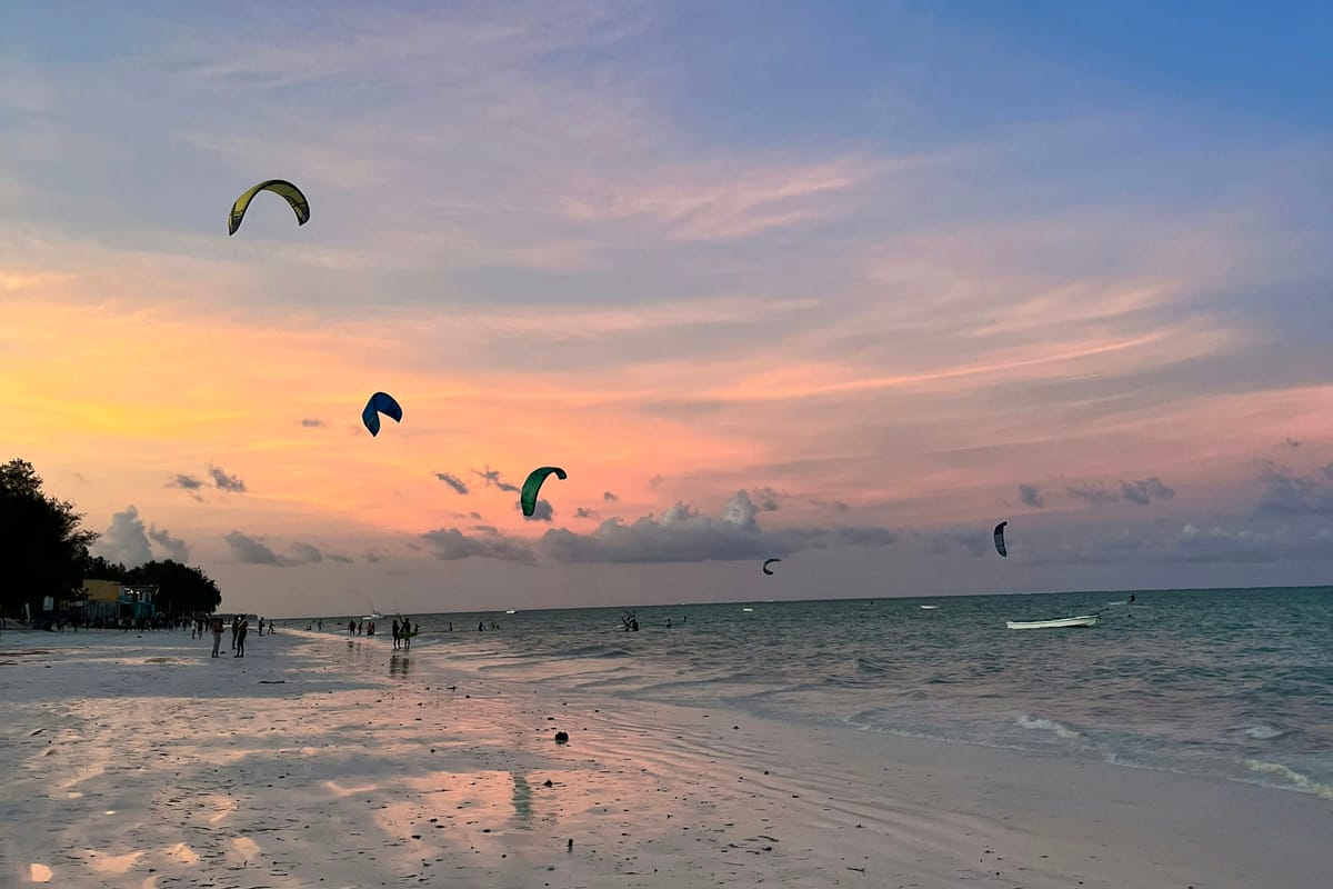 Kitesurferi nad pobrežím Zanzibaru pri ružovom západe slnka