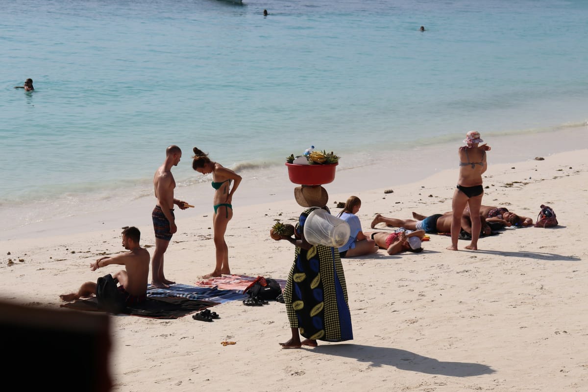 Predavačka s košom ovocia na hlave medzi turistami na pláži v Nungwi